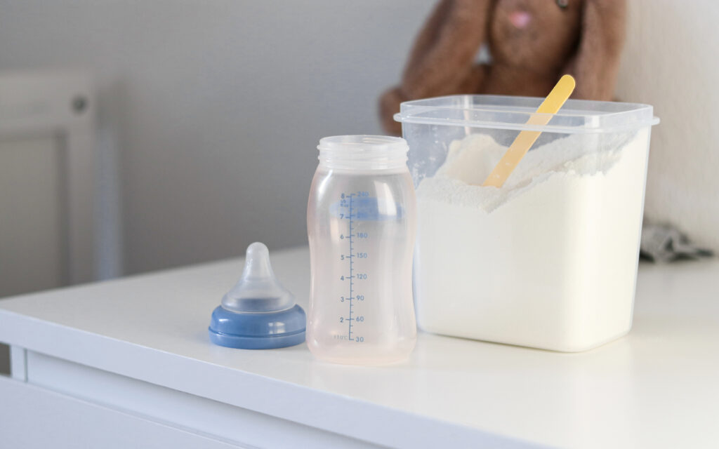 A container of baby formula with an empty bottle.