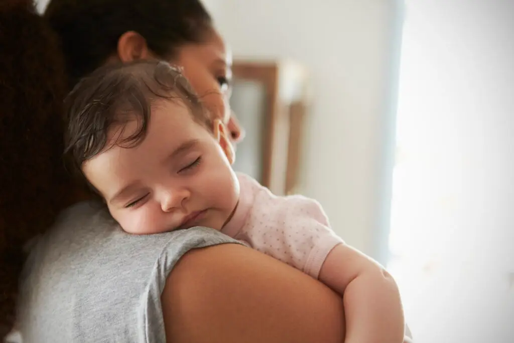 A baby sleeping on their mother's shoulder.